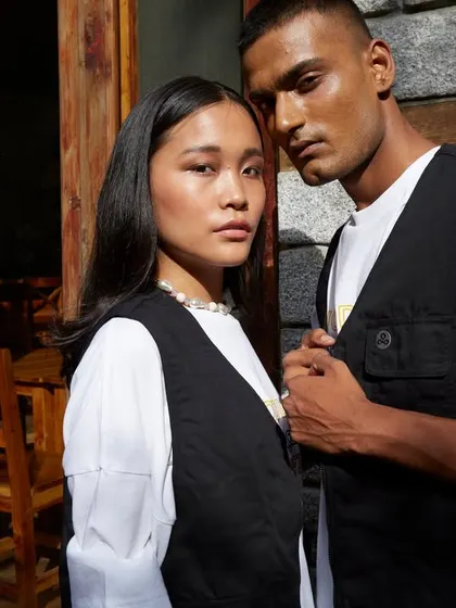 A campaign image for Woodland's "A Skating Monk" collection. The shot captures a quiet, intimate moment between the two models, with the natural light and rustic setting reflecting the brand's connection to nature and urban culture.