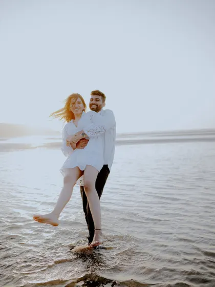 A playful and spontaneous moment captured at the beach. The groom lifting the bride as they stand in the water is full of energy and laughter, showing the fun side of their relationship.