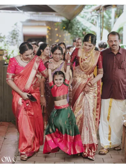 A heartwarming candid moment as the bride walks with her family, a young flower girl playfully swinging from her hand.