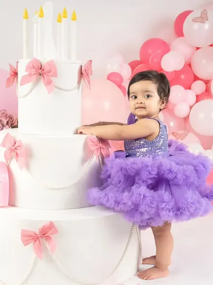 This little girl in her purple dress stands next to a giant prop cake, making her look like a tiny princess in a fairytale.