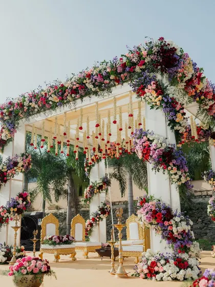 A closer look at the stunning floral arrangements on our outdoor wedding mandap, showcasing a rich mix of colors and textures against the bright blue sky.