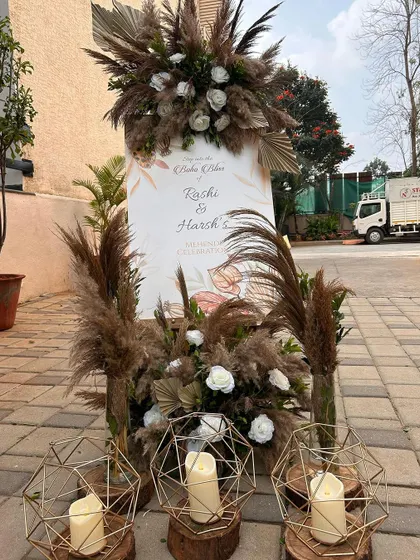 A boho welcome sign for a Mehendi ceremony, featuring dried pampas, white roses, and geometric candle holders for a rustic yet elegant feel.