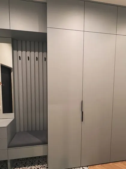 This shot showcases the full length of the integrated entryway wardrobe. The floor-to-ceiling design provides ample storage, while the adjacent seating and mirror unit adds everyday convenience.