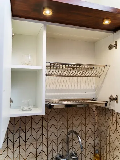 A practical dish-drying rack installed inside an overhead cabinet. This clever design keeps your counter space clear and allows dishes to drip-dry directly into the sink area, maintaining a clean and organized kitchen.