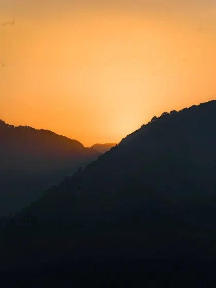 A minimalist photo of the sun setting behind the hills of Mussoorie. The simple silhouette and the vibrant orange sky create a powerful and artistic landscape shot.