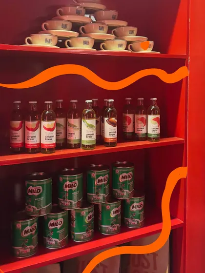 The colorful shelves of a cafe, with an orange squiggle to complement the red and green of the Milo cans.