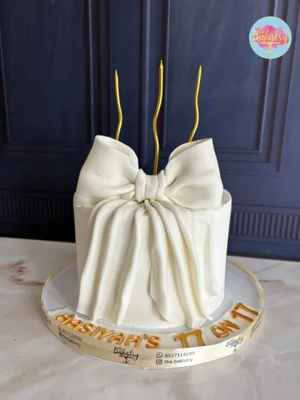 A stunning draped bow cake for Aasiyah’s 17th celebration. This elegant creation features a beautifully sculpted white bow and golden candles for a touch of class.