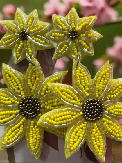 Another look at these sunny yellow floral earrings, set against a soft pink background. The detailed beading on each petal and the dark center create a lovely contrast.