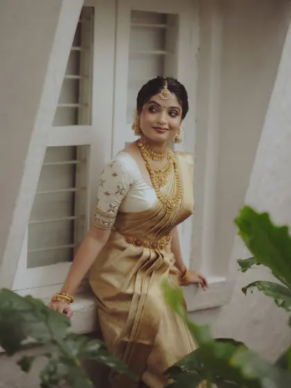A beautiful three-quarter portrait of a bride in a golden saree, posing by a window.