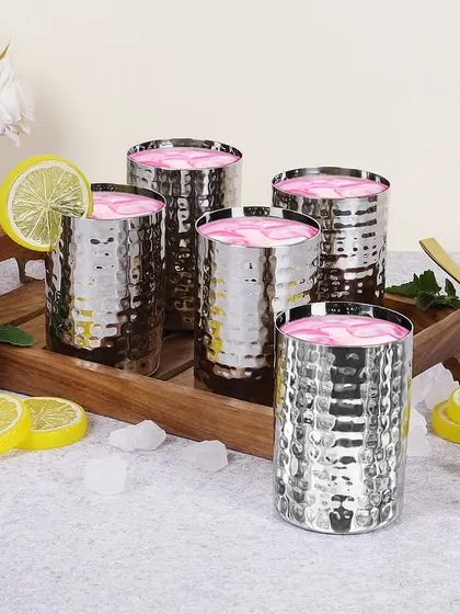 A beautifully styled shot of hammered steel glasses filled with a pink drink. The wooden tray, lemon slices, and ice cubes create a refreshing and appealing scene, perfect for a summer beverage.