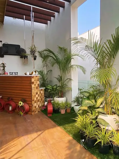 This balcony in Faridabad features a custom bar counter, wooden flooring, and an abundance of potted plants, creating a perfect spot for entertaining.