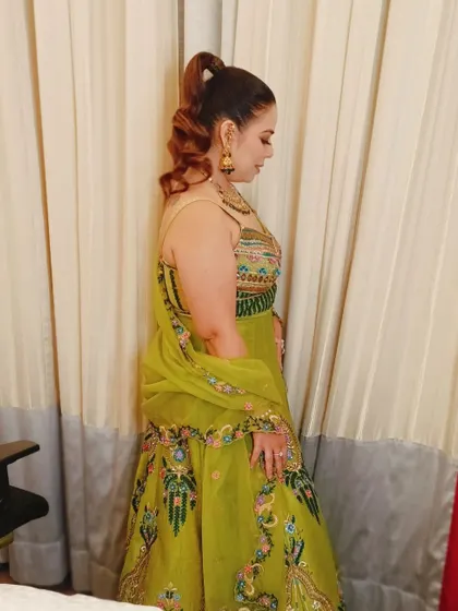 A side view of the client's high ponytail, showing the volume and texture of the curls. This is a glamorous and comfortable style for any festive occasion.