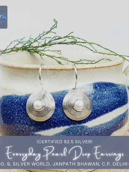 These modern-ethnic drop earrings have a pearl at the center of a textured, spiral-patterned silver disc, offering a contemporary take on classic pearl jewelry.