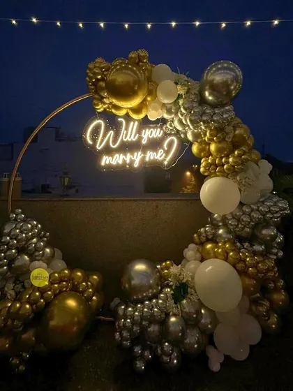 Our rooftop proposal setup under the night sky. The circular arch adorned with gold, silver, and white balloons and a bright neon sign creates a stunning focal point for a magical question.