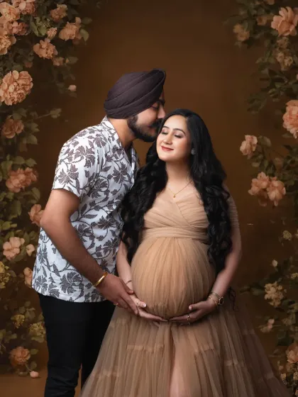 A tender moment in a floral wonderland. The father-to-be gently kisses his partner's cheek, surrounded by a beautiful arch of rustic-toned flowers.