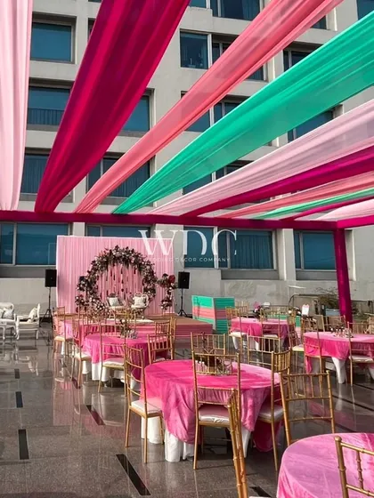 The rooftop venue was transformed with a canopy of vibrant drapes in shades of pink, magenta, and teal, creating a colorful and festive atmosphere for the Mehendi.