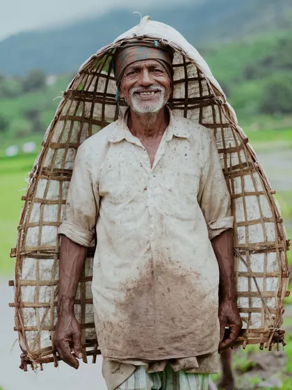 A heartwarming portrait of a smiling farmer in Junnar, carrying a traditional bamboo rain shield ('irle'). This image captures the simple joy and resilience of life in the Ghats during the monsoon.