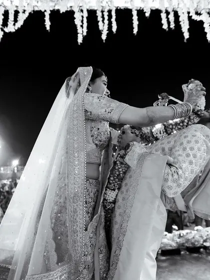 A dynamic black and white shot of the Varmala ceremony, capturing the fun moment the groom is lifted up by his friends. It's a perfect candid of wedding fun.