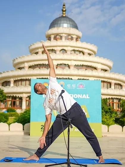 An instructor demonstrates Trikonasana (Triangle Pose) with the Vishalakshi Mantap in the background. Our yoga teacher training programs focus on mastering asanas and understanding the deeper philosophy of yoga.