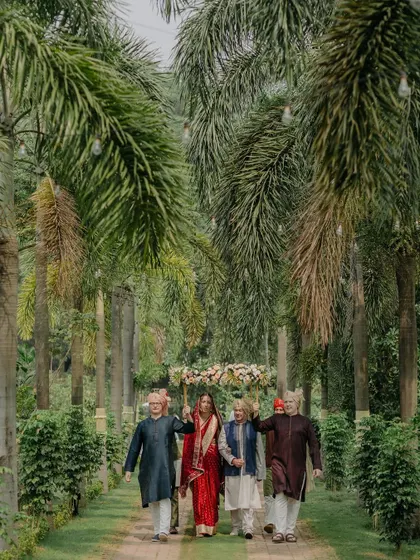 The bride's serene walk to the mandap through a pathway of palm trees, holding hands with her family, a beautiful and calm bridal entry.