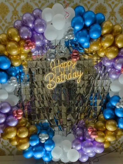 A vibrant birthday backdrop with a silver shimmer panel surrounded by a colorful ring of balloons in blue, purple, and gold.