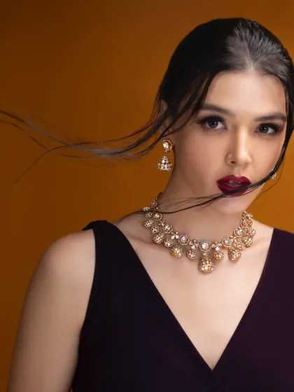 A close-up beauty shot with a focus on movement. The windswept hair adds a dynamic element to this portrait, drawing attention to the elegant necklace and the model's bold expression.