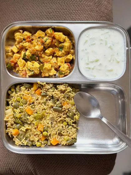 A delicious meal of vegetable pulav with paneer bhurji and a side of cucumber raita.