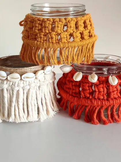 An assortment of three macrame jars, featuring different colors, patterns, and shell embellishments.