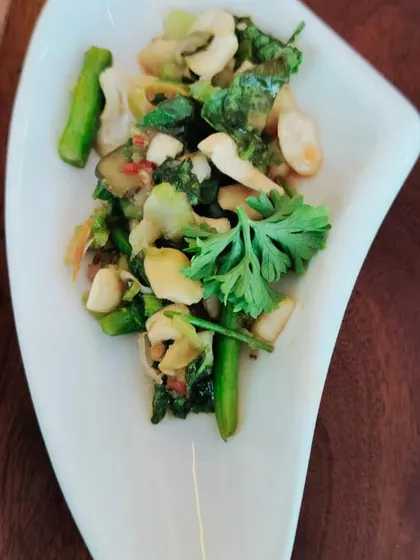 A healthy and flavorful stir-fry salad with broccoli, cashews, and fresh cilantro, presented in a modern, curved dish.