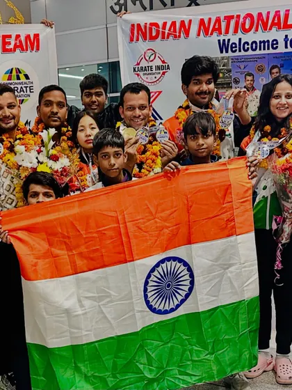 The victorious Indian karate team welcomed at the airport, holding the national flag and displaying their medals from the Commonwealth Championship. The joy of returning home as champions is unmatched.