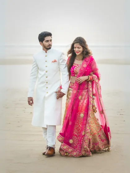 A lovely portrait of a couple walking on the beach in their traditional wedding outfits. The natural light and serene background make this a timeless and romantic image.