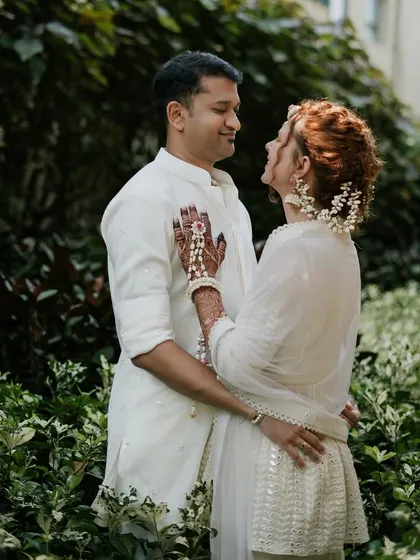 A sweet moment between the couple in their matching ivory Haldi outfits, surrounded by lush greenery. The floral jewelry adds a delicate pop of color to the bride's look.