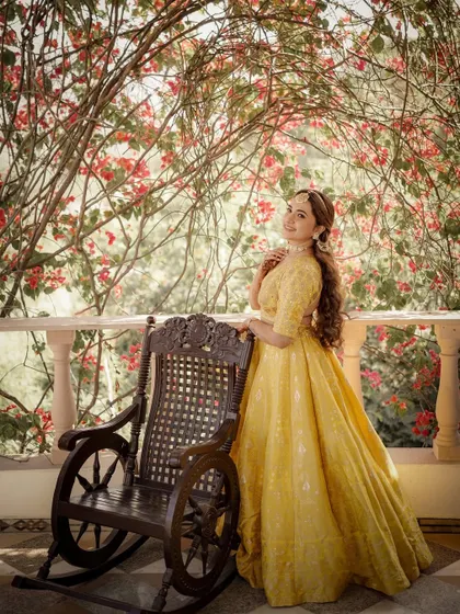 The bride in her yellow lehenga, posing by a rocking chair and a wall of bougainvillea, creating a beautiful, classic portrait.