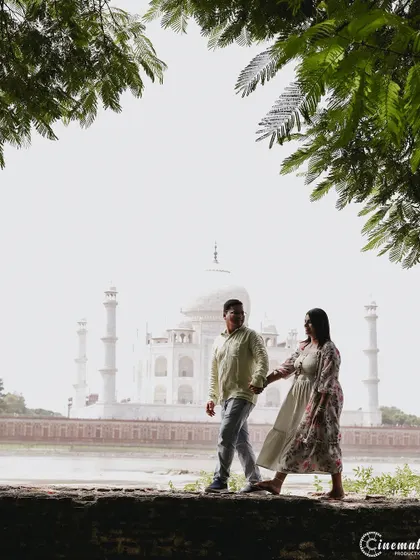 A candid walking shot with the Taj Mahal in the background. The natural frame of the tree leaves adds an artistic touch, making it feel like a stolen moment in a grand love story.