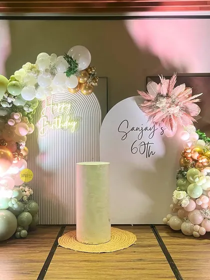 A sophisticated setup for Sanjay's 60th birthday. We used a soft color palette with sage green and peach balloons, elegant white arched backdrops, and pampas grass for a refined and modern look.