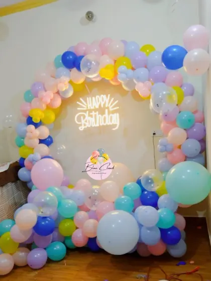 A vibrant pastel rainbow balloon ring with a 'Happy Birthday' neon sign.
