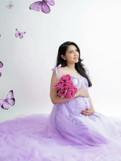 A whimsical portrait with purple butterflies. The mom-to-be, in a matching lavender gown, looks up as if watching them fly, creating a magical scene.