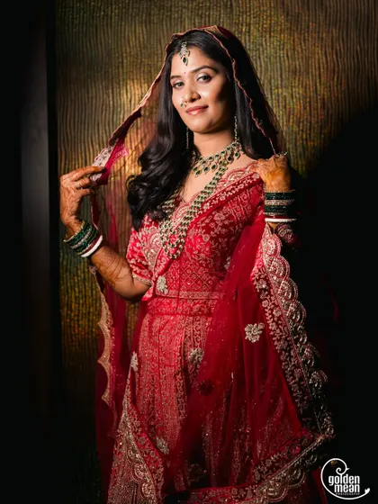 A stunning portrait of a bride in a rich red lehenga, holding her veil.