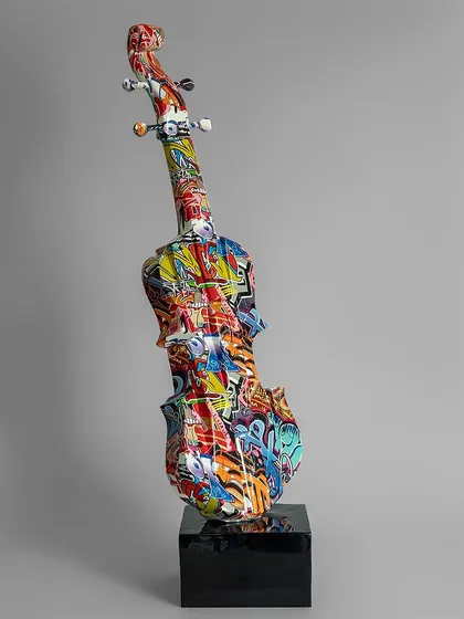 A full-size violin sculpture is transformed into a modern art piece with a dynamic graffiti finish. Mounted on a black pedestal, it's a statement piece that celebrates both music and contemporary art.
