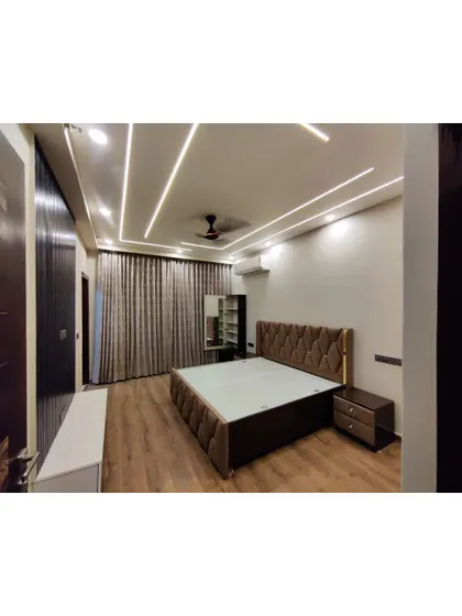 This bedroom features a rich, tufted headboard and warm wood flooring. The false ceiling with integrated linear lighting adds a contemporary touch to the otherwise classic and comfortable room.