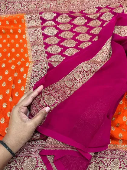 The plain rani pink blouse piece for the orange Kadi georgette saree, highlighting the detailed floral border.