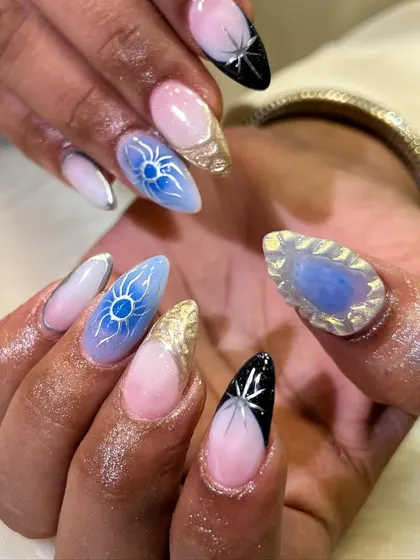 Celestial dreams. This intricate nail art features sun and star motifs with a mix of blue ombre, gold foil, and a stunning 3D gem accent nail.