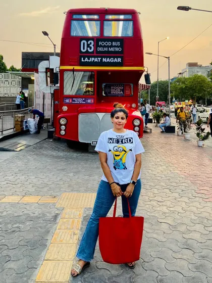 A casual summer look with a Minions graphic tee and flared jeans, posing in front of a cool red double-decker food bus in Delhi.