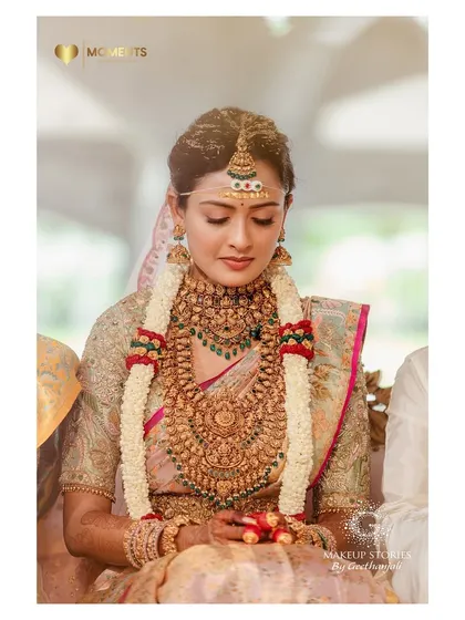 Ashitha during her wedding rituals. Her makeup is subtle and elegant, with a focus on flawless skin, allowing the traditional jewelry and rituals to be the highlight.