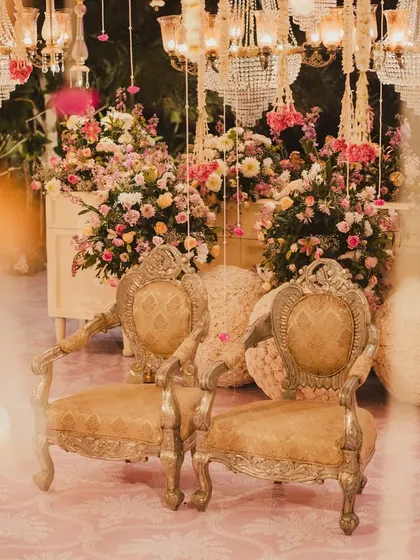 The mandap seating, with its ornate golden chairs, is set amidst a profusion of flowers and glittering chandeliers, creating a space fit for royalty.