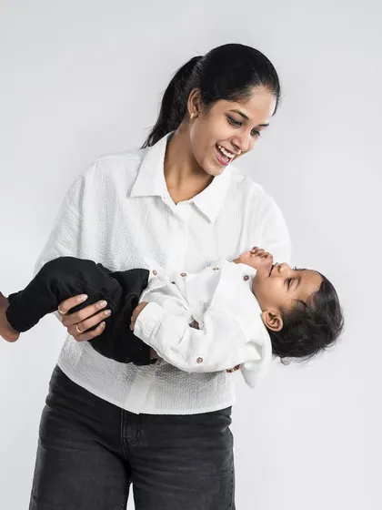 A mother joyfully holds her baby, their matching outfits and bright smiles creating a light and happy atmosphere in the studio.