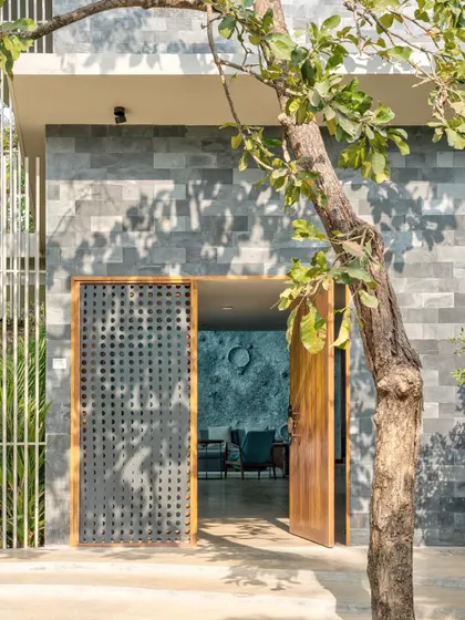 The entrance to the Moon House features a facade of cool grey stone and a perforated metal screen. This material combination, framed by a mature tree, creates a welcoming threshold that hints at the artistic interiors within.