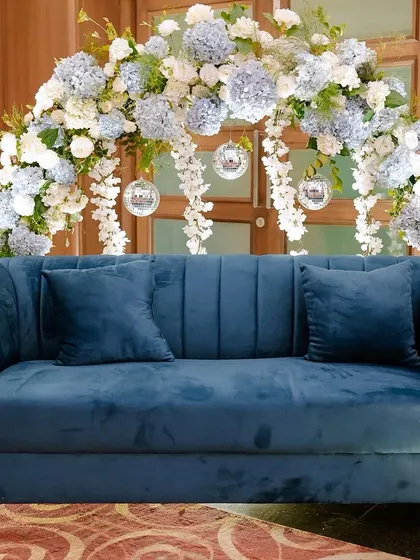 The full photo booth setup for the Sangeet, featuring a plush blue sofa set against a stunning arch of hydrangeas and disco balls. It was a popular spot for photos all night long.