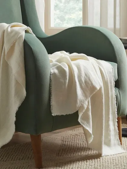 A soft, cream-colored throw blanket draped casually over a green armchair. This shot focuses on creating a feeling of comfort and relaxation.
