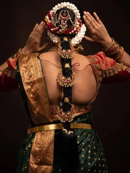 A bride adjusting her hair, which is beautifully decorated with flowers and a traditional jada with chandbali-style pieces.
